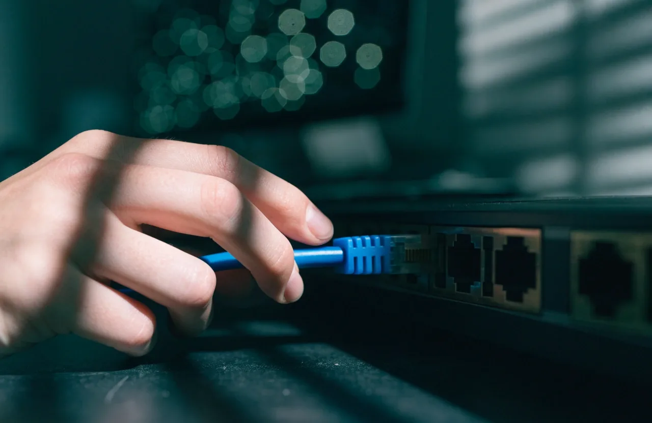 Hands plugging a patch cable into a switch port at a workbench in cool light